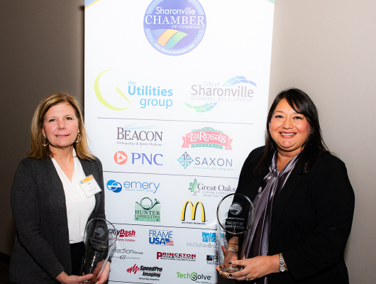 two women standing in front of sign holding awards